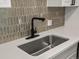 Close-up of the kitchen sink with sleek fixtures and unique tile backsplash at 2500 S York St # 204, Denver, CO 80210