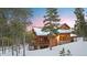Log home with stone accents, snow covered roof, and a wraparound deck in a wooded area at dusk at 378 Juniata Cir, Breckenridge, CO 80424