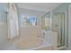 Bathroom with a jacuzzi tub and glass-enclosed shower, all surrounded by white tiling and natural light at 2364 S Harlan St, Lakewood, CO 80227