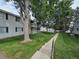 Low-angle exterior of apartments with lush green lawns, mature trees, and gray siding accented by stone chimney and dark shutters at 14433 E Jewell Ave # 101, Aurora, CO 80012