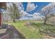 Backyard view of a grassy yard, brick fire pit, and scattered trees underneath a cloudy sky at 7715 Rafter Rd, Franktown, CO 80116
