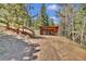 Carport and parking area surrounded by pine trees, with wooden stairs leading up to the home at 32187 Sylvan Rd, Golden, CO 80403