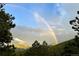 A stunning rainbow stretches across the sky over a mountain range, framed by green trees at 32187 Sylvan Rd, Golden, CO 80403