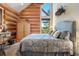 Cozy bedroom featuring a large bed, rustic wooden walls, and a large window with views at 8699 Blue Creek Rd, Evergreen, CO 80439