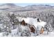 Charming log home with snow-covered roof, surrounded by snow-covered pine trees, creating a serene and picturesque winter scene at 8699 Blue Creek Rd, Evergreen, CO 80439