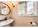 Powder room with pedestal sink, round mirror, modern fixtures, and natural light at 4645 W Temple Pl, Denver, CO 80236