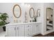 Bright bathroom with dual sinks, white cabinets, wood look floors, two mirrors, and brass hardware at 10938 Mcclellan Rd, Parker, CO 80134