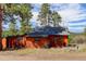 Rustic log cabin with a gray roof, surrounded by trees and with a view of snow-capped mountains in the distance at 6743 Wild Rose Ln, Evergreen, CO 80439