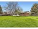 Large grassy backyard featuring mature trees, brick house and glass enclosed sunroom at 798 Alkire St, Lakewood, CO 80401