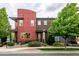 Modern townhome showcases a brick and red exterior, small yard with lush greenery at 2110 W 67Th Pl, Denver, CO 80221