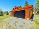 Exterior view of a wooden, two-car garage with a black door in a grassy and gravel lot at 29590 Buchanan Dr, Evergreen, CO 80439