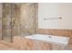 A bathroom featuring travertine tile, a glass shower enclosure, and a soaking tub, exuding warmth at 2400 E Cherry Creek South Dr # 207, Denver, CO 80209