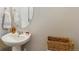 Powder room featuring pedestal sink, oval mirror, and a stylish wicker basket atop the toilet at 1954 S Poplar Ct, Denver, CO 80224
