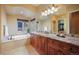 A bathroom with a tub, granite counters, wood cabinets, and a large mirror with views of the trees at 18720 Lake Dr, Monument, CO 80132