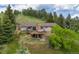 Aerial view showcases a backyard with an elevated deck, hot tub, and mature trees on a lush hillside at 24030 San Isabel Rd, Indian Hills, CO 80454