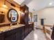 Elegant bathroom featuring granite countertops, dark wood cabinets, and a large round mirror at 10895 Pheasant Run, Littleton, CO 80125