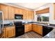 Kitchen featuring wood cabinets, granite countertops, black appliances and window with a view at 9610 S Dover Way, Littleton, CO 80127