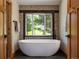 Close up of a soaking tub next to a picture window, with wood trim and stone accents in this luxury bathroom at 31756 Buffalo Park Rd, Evergreen, CO 80439