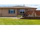 A partially fenced backyard with green grass, rock area, small patio, and flowers with a view of the home's exterior at 16141 W 64Th Way, Arvada, CO 80007