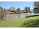 Scenic backyard view of a waterfront property with a lush green lawn, pond, and mature trees on a sunny day at 4323 W Ponds Cir, Littleton, CO 80123