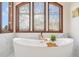 Elegant soaking tub with gold fixtures beneath arched window, set against marble wall and floors at 6180 E Quincy Ave, Cherry Hills Village, CO 80111