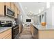 Open kitchen view featuring stainless appliances, wood cabinets, hard surface countertops, and a living area in the background at 5319 Warrior St, Frederick, CO 80504