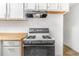 Classic kitchen featuring a gas range with a hood vent, white cabinets, and butcher block countertops at 540 Hickory St, Hudson, CO 80642