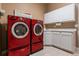 Bright laundry room with red washer and dryer set, white cabinets, and white countertop with a sink and a flower painting at 4275 S Dawson St, Aurora, CO 80014