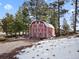 Charming red barn with white trim, nestled amidst trees and snow patches, adding rustic appeal to the property at 3945 Douglas Mountain Dr, Golden, CO 80403