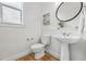 A bright, white powder room with a pedestal sink, round mirror and wood-look floors at 9826 E 27Th Dr, Denver, CO 80238