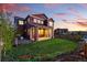 Inviting backyard featuring a manicured lawn, flowers, and a two-story red home at dusk at 4825 Basalt Ridge Cir, Castle Rock, CO 80108