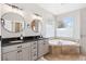 Bathroom with dual sinks, dark countertops, neutral cabinets, soaker tub, and two large windows at 3048 Deer Creek Ranch Loop, Parker, CO 80138