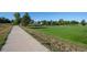 A sunny green neighborhood park with a concrete path, manicured grass lawn, and mature trees at 5481 E 117Th Ave, Thornton, CO 80233