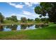 A tranquil pond, adorned with lush green grass, rocks, and mature trees reflects the sky in the community at 5481 E 117Th Ave, Thornton, CO 80233