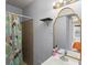 Bright bathroom with a cactus shower curtain, a tan tiled shower wall, and an ornate mirror with a shelf and toiletries at 1670 Oakland St, Aurora, CO 80010