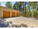 Exterior view of a three-car garage with wood doors, a large parking area, and mature trees at 1250 Dolan Dr, Monument, CO 80132