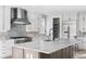 Bright kitchen featuring white cabinetry, marble countertops, a stainless steel range hood, and an island sink at 6529 Still Pine Cir, Castle Pines, CO 80108