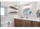 Bathroom with a wood vanity, gold hardware, a round mirror, and open shelving at 2570 Bell Ct, Lakewood, CO 80215