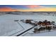 Stunning aerial view of a snow-covered property with multiple outbuildings and mountain views at sunset at 4075 Merada Ct, Franktown, CO 80116