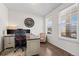 Well-lit home office with hardwood floors, dual monitors, decorative wall clock, and neutral-toned decor at 14275 Grape St, Thornton, CO 80602