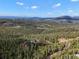Expansive aerial view of a home nestled within a lush forest with mountains and a blue sky in the distance at 29825 Kennedy Gulch Rd, Conifer, CO 80433