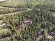 A serene aerial view shows a brown house nestled in a dense forest with a winding driveway at 29825 Kennedy Gulch Rd, Conifer, CO 80433