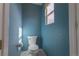 Cozy blue bathroom featuring a white toilet, wall paper holder and a window bringing in natural light at 9703 Ogden Ct, Thornton, CO 80229