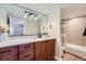 Bright bathroom with a wood vanity, stone countertop, bathtub with tiled shower, and modern decor at 960 Promontory Cir, Elizabeth, CO 80107