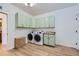 Laundry room with modern washer and dryer units, light green cabinets, and a sink at 960 Promontory Cir, Elizabeth, CO 80107