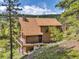 Secluded log cabin featuring an outdoor deck and stone chimney, surrounded by lush greenery and towering trees at 1000 Lodgepole Dr, Evergreen, CO 80439