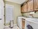 Bright laundry room featuring a modern washer/dryer, wooden cabinets, and a stainless steel trash can at 1540 W Briarwood Ave, Littleton, CO 80120