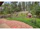 Landscaped backyard with stone patio, fireplace, mature trees, waterfall, and a sloping hillside at 29832 Dorothy Rd, Evergreen, CO 80439