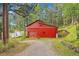 Quaint red barn with garage door, small trailer, and gravel driveway surrounded by grassy area and tall trees at 29832 Dorothy Rd, Evergreen, CO 80439