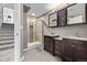 Bathroom featuring a glass door shower, wood cabinets, dual sinks, and modern tile at 7586 Halleys Dr, Littleton, CO 80125